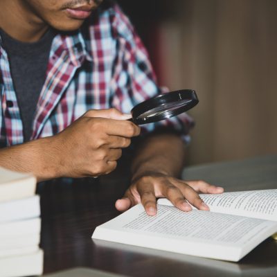 Educational theme: Close -up Student looking through a magnifying glass to  book
